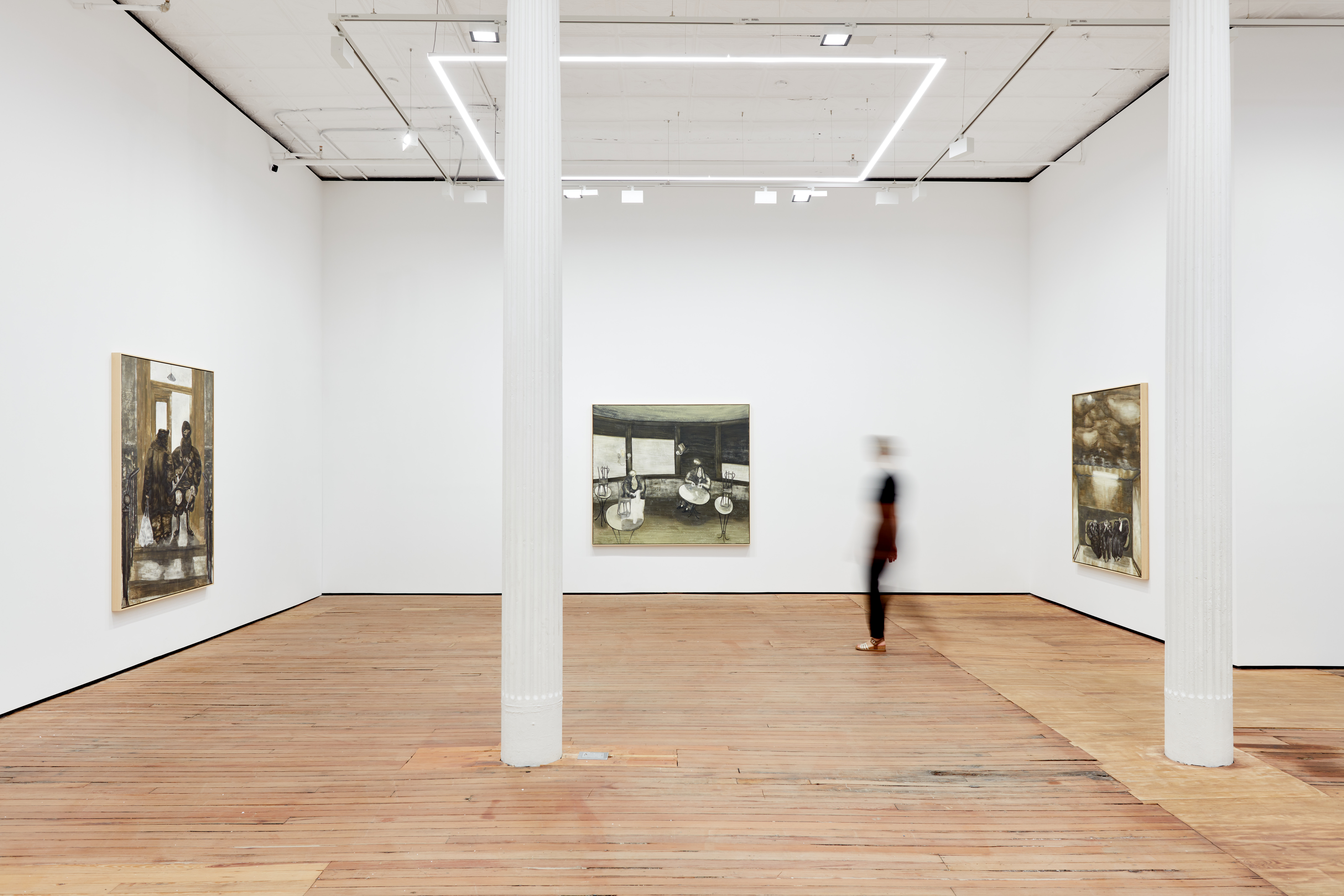 A blurry viewer walking in an art gallery with 3 large paintings exhibited on white walls.