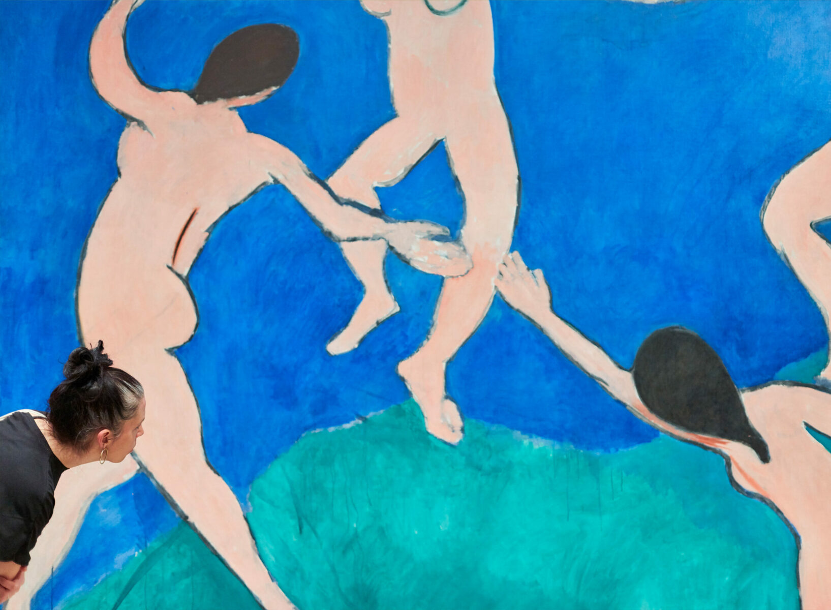 A viewer in front of Henry Matisse's painting "Dance (I)". The artwork shows multiple naked figures dancing in a green and blue background.
