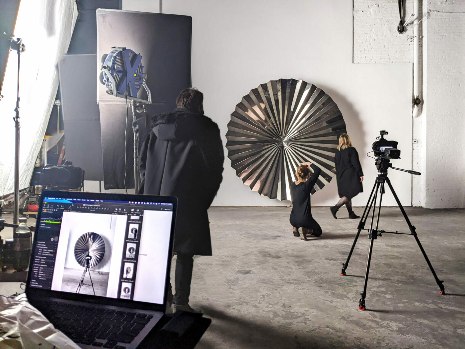 A behind the scenes video production with tripods, lights and a large metal rounded sculpture. 