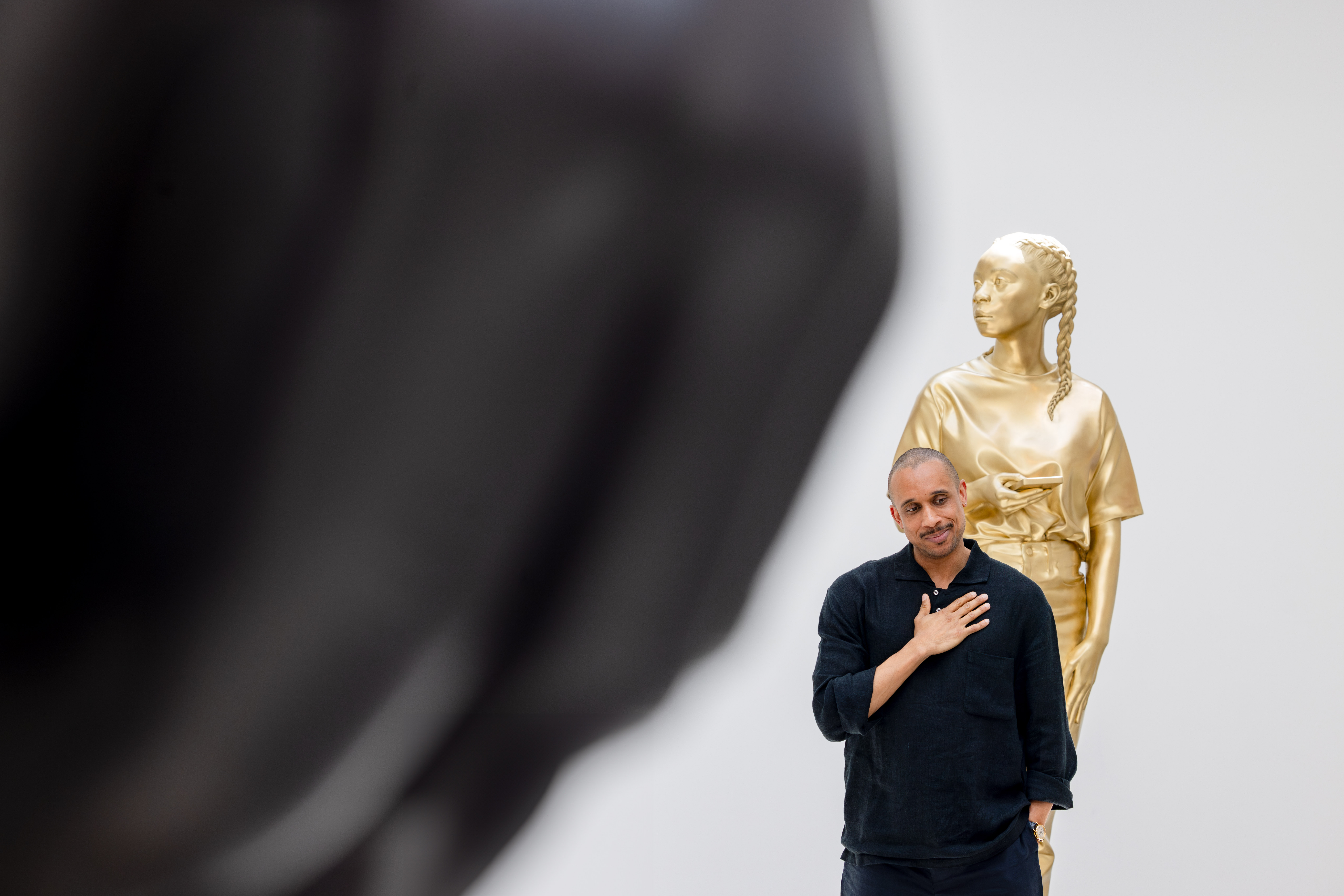 Artist Thomas J Price in front of one of his large golden human sculptures.