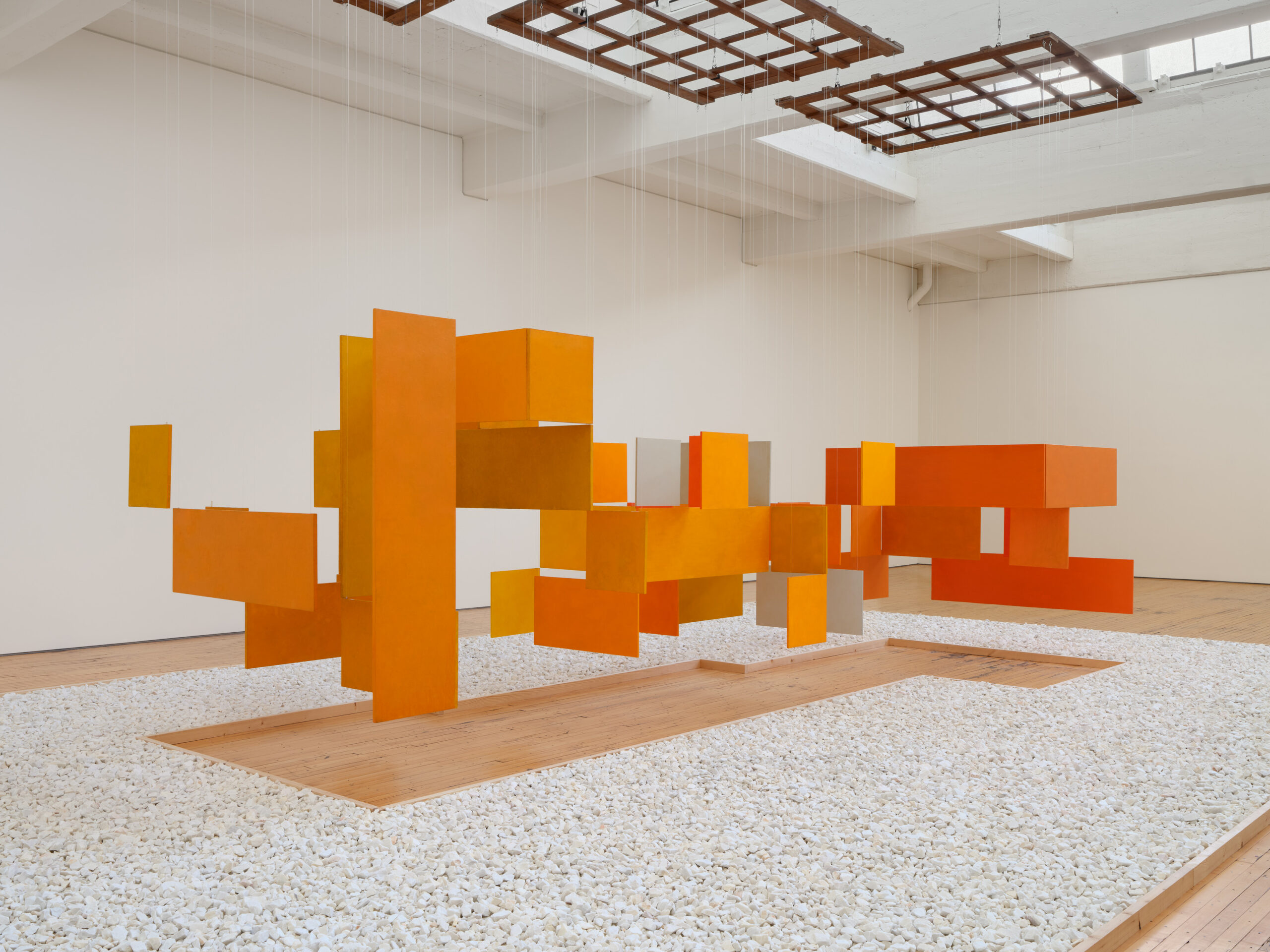 a large sculptural installation of orange, ocher and grey rectangular panels suspended vertically from the ceiling.