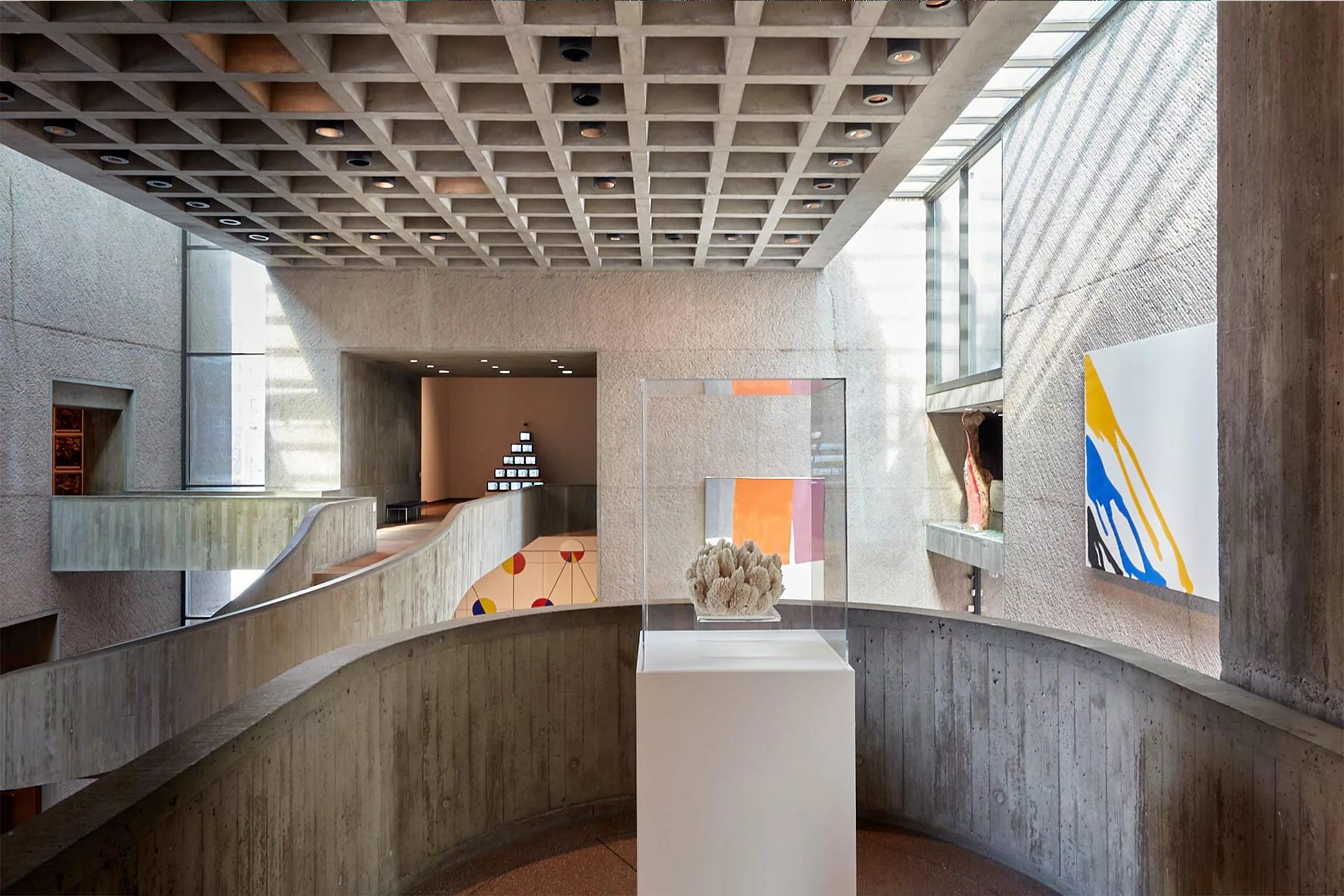 Exhibition photograph of an architectural view of the interior of a museum with concrete walls and multiple artworks on display.