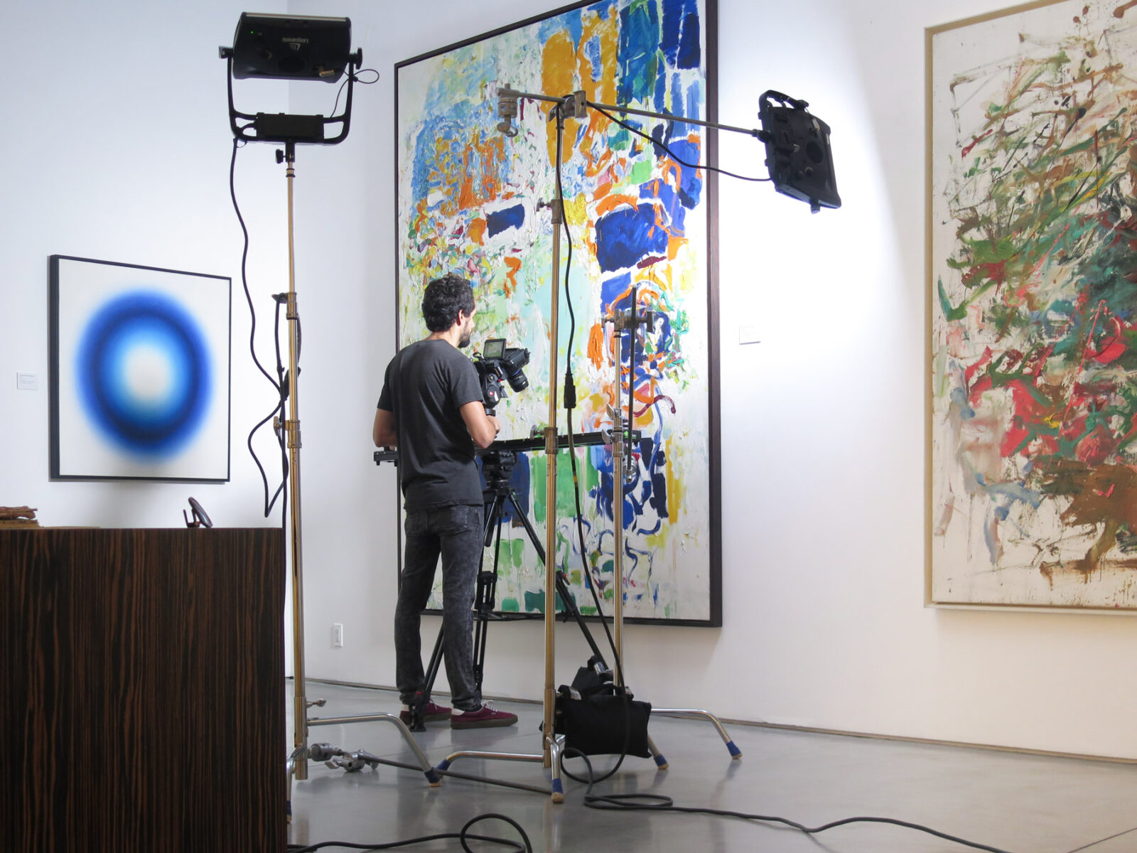 Video Artwork documentation. BTS of a cinematographer shooting a large painting with lights on stands and a slider.