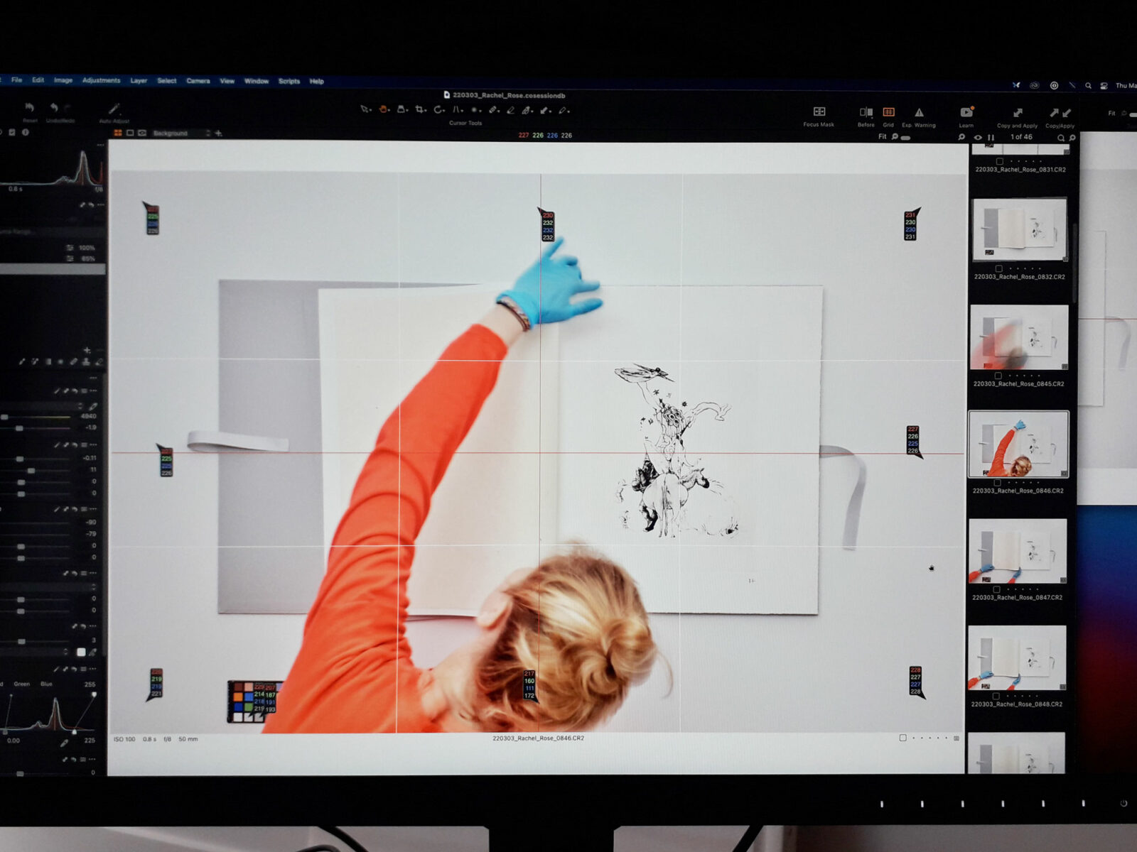Photo shoot tethered to a monitor displaying an overhead view of a oversize book and a person with gloves adjusting the position of a page.