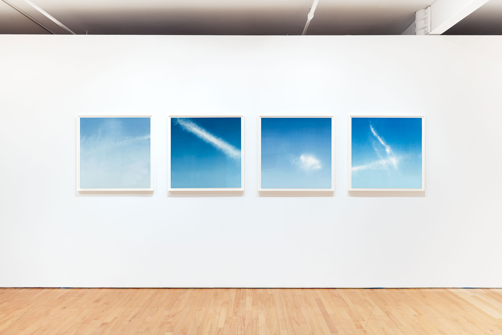 Four pictures of dark blue skies with white clouds installed in and art gallery.