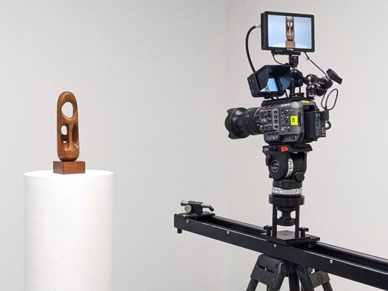 Film recording of a wooden sculpture by Elizabeth Catlett placed on a pedestal. The cinema camera is rig into a slider and has two small monitors on the top.